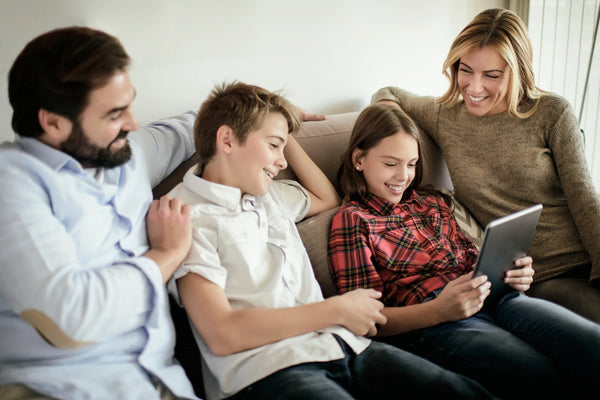 Familie mit zwei Kindern sitzt entspannt auf dem Sofa und schaut gemeinsam auf ein Tablet